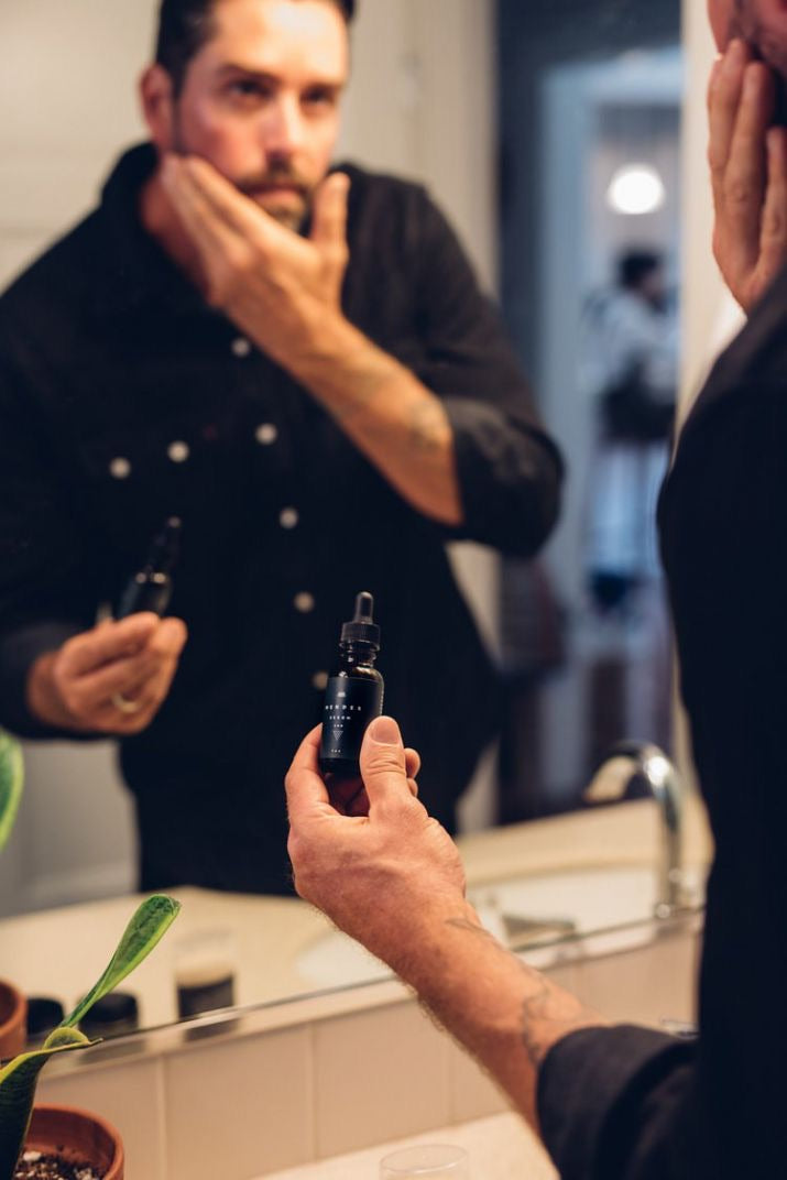 man using cbd beard lotion at the mirror